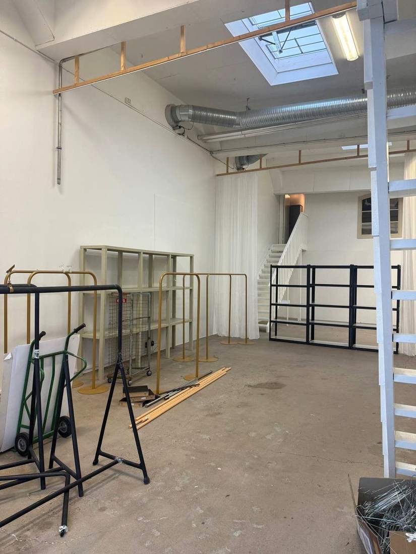 Ljus studioyta med vita draperier, betonggolv och takfönster